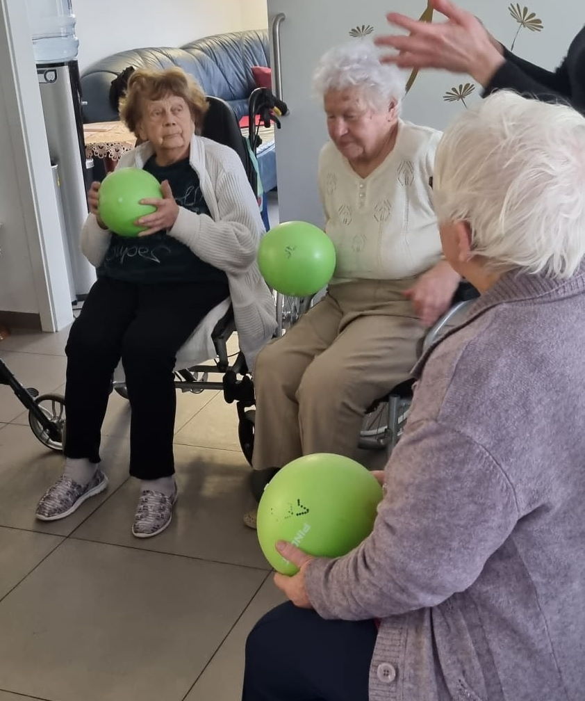 Bewohner der Wohngemeinschaft sitzen zusammen und machen Sportübungen mit einem Ball