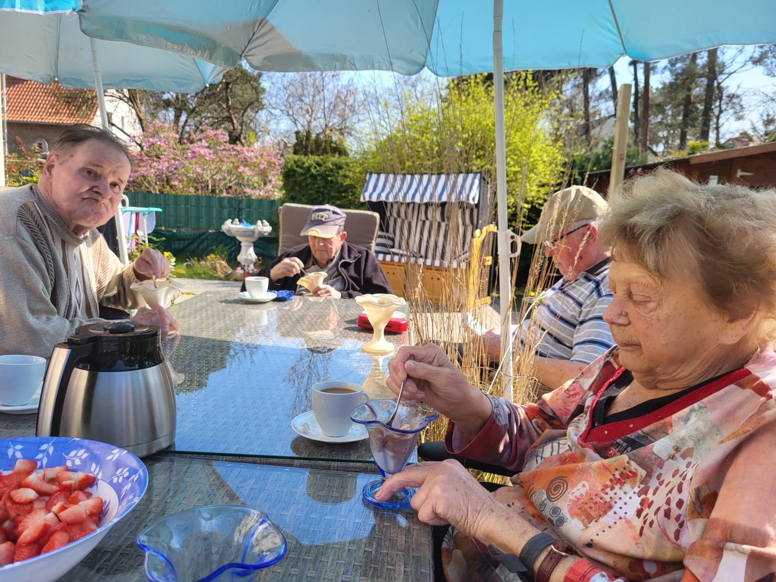 Bewohner der Wohngemeinschaft sitzen am Gartentisch und essen Eis und Erdbeeren