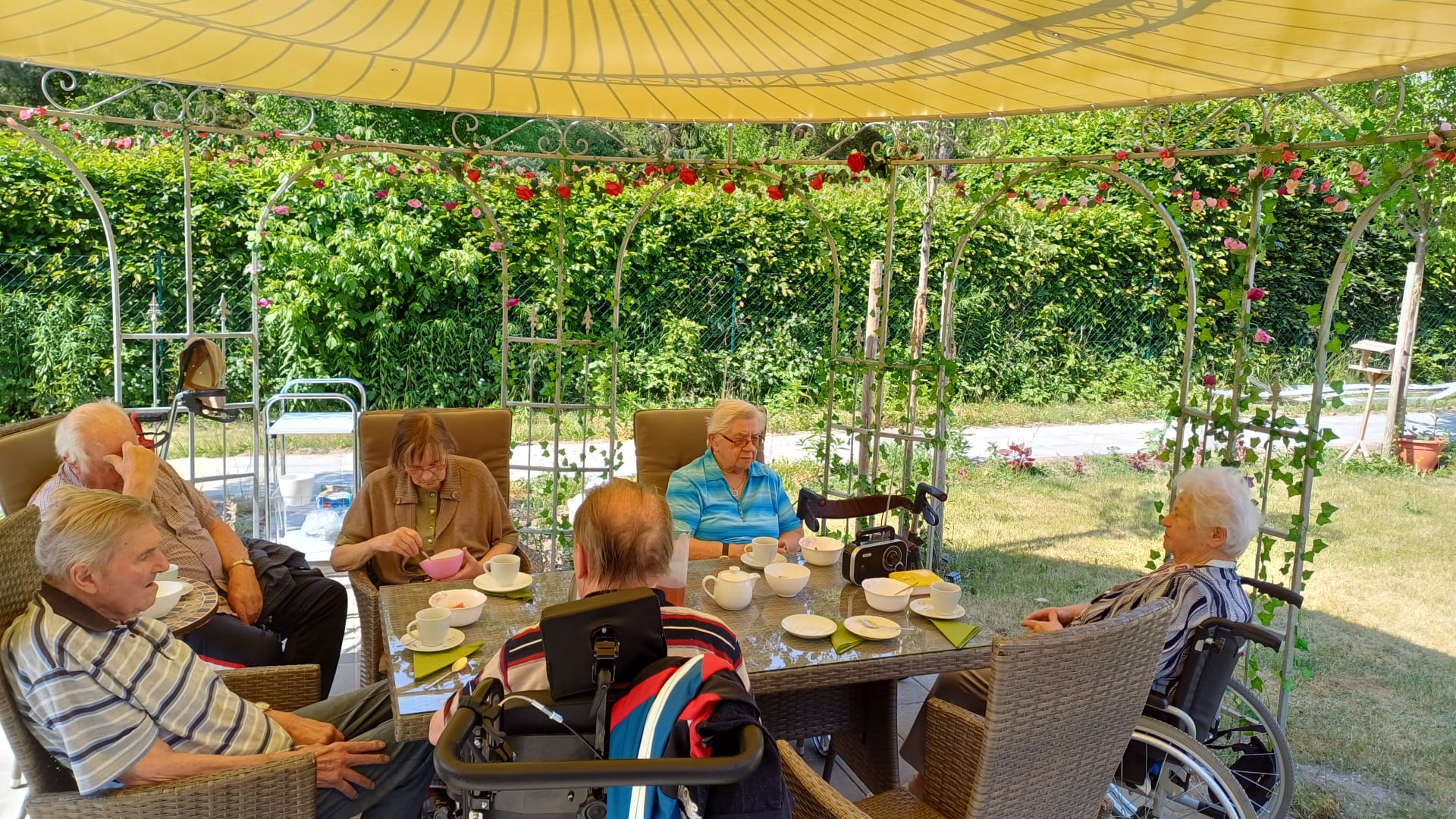 Bewohner der Senioren Wohngemeinschaft Haus Oldenburg sitzen unter dem neuen Pavillon bei einem Kaffee